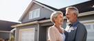 Elderly married couple celebrating their new home standing in front and proudly displaying keys